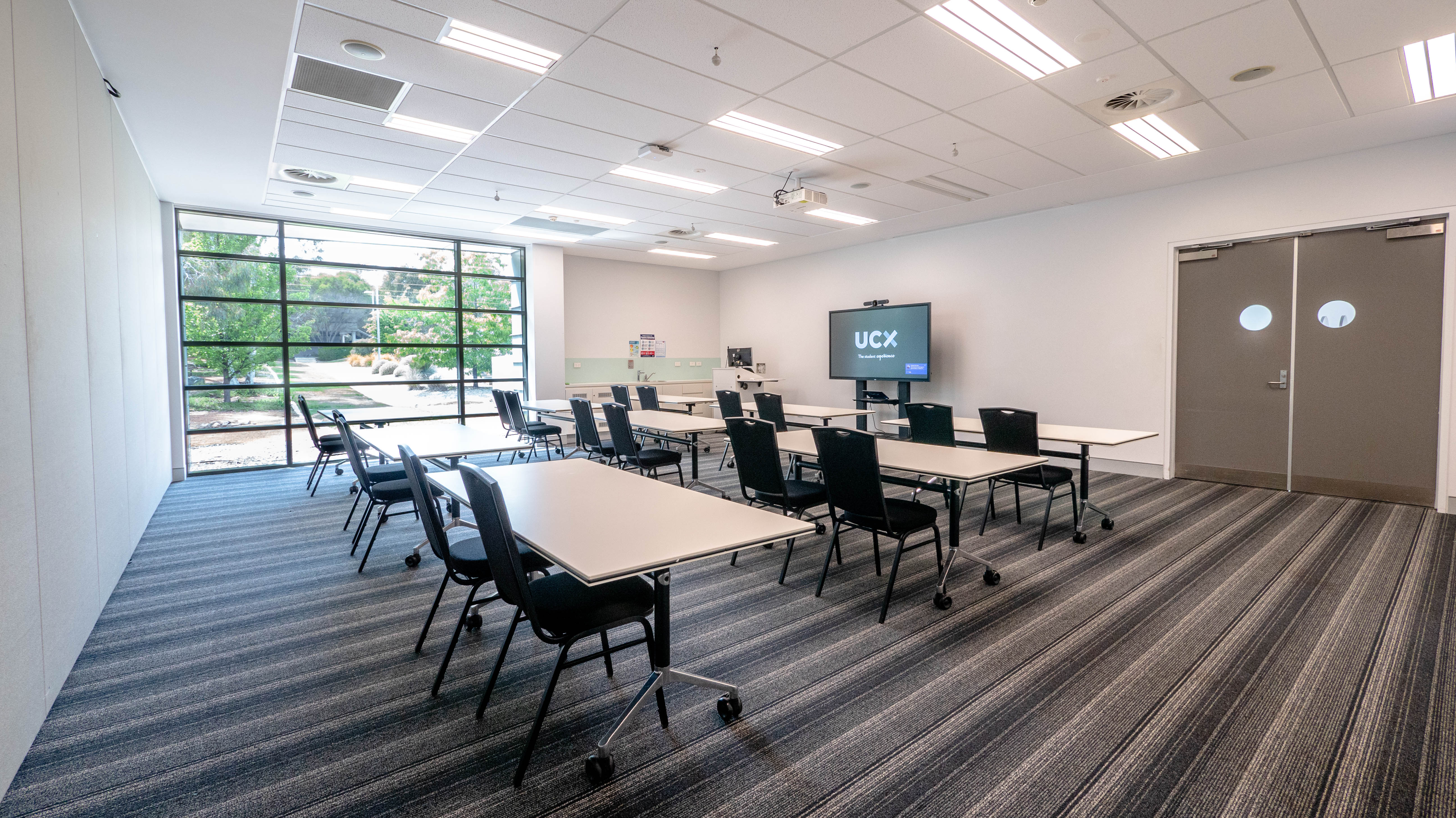 Ann Harding Conference Centre seminar room set up with blue chairs and tables in a classroom style. The chairs and tables face a television displaying the UCX logo