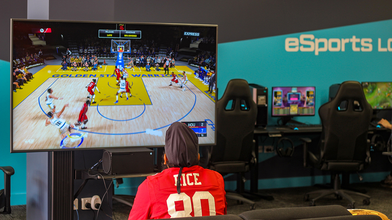 One male student facing a television and playing xbox. The student is playing a virtual sporting game. 