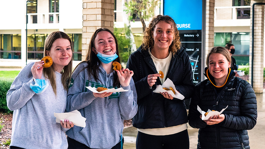 Four female students smiling and holding cinnamon donuts.