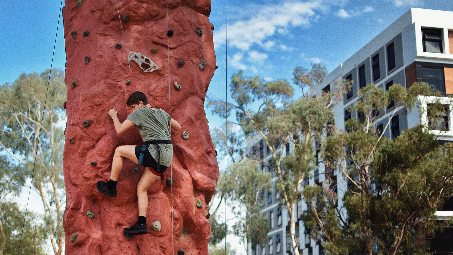 Male student half way through climbing upright mobile rock wall.