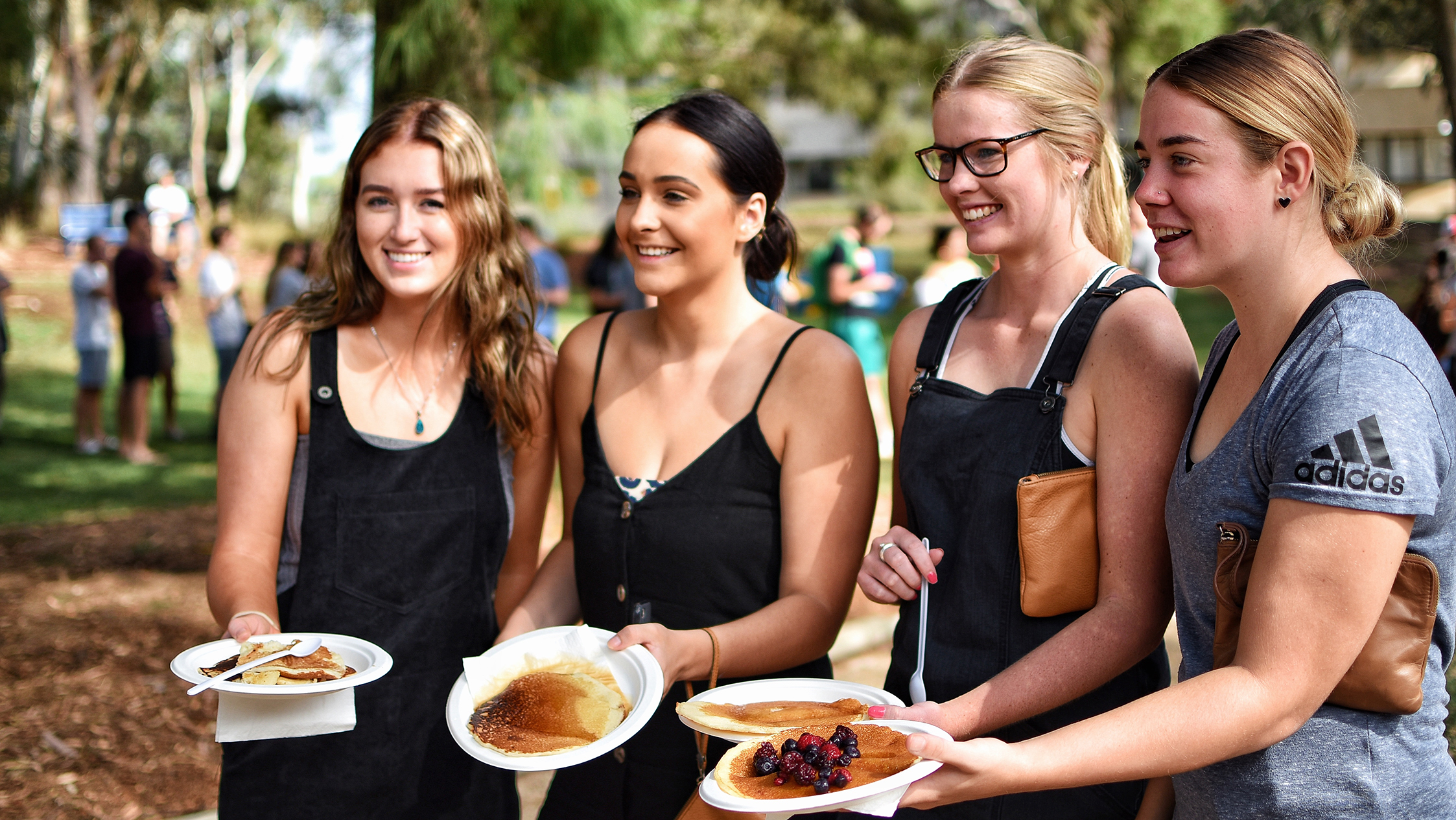 Four female students smiling and showing plates with pancakes outside at an O-Week event.