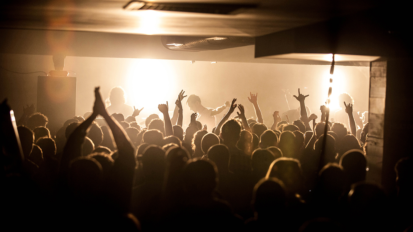 Crowd seen as silhouettes at a concert at the UC Hub, performers on stage are obscured by bright golden lights. 