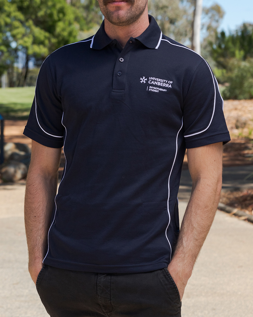 The torso of a male student. He is wearing a dark navy polo with white piping. The polo features a University of Canberra Logo on the left side just above the chest. Underneath this, white text reads physiotherapy student