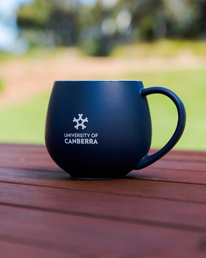 A rounded navy mug featuring a white University of Canberra logo.